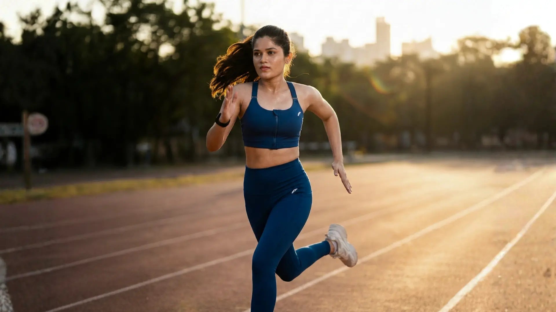 Athletic woman in blue full coverage sports bra and leggings running on an outdoor track during sunrise workout in India
